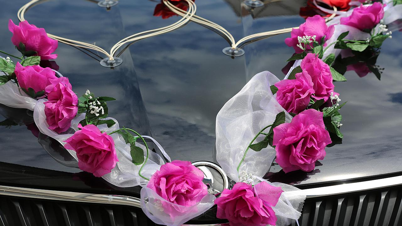 Herzen und Blumen für Eheschließung auf Motorhaube eines Autos
